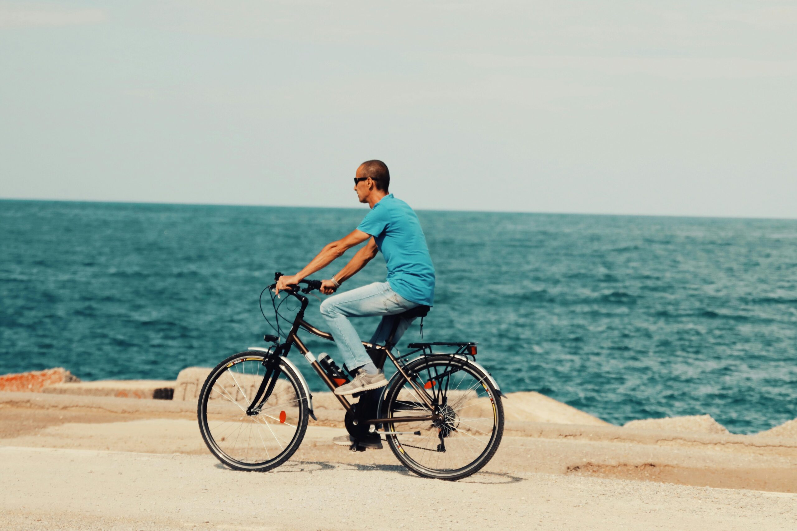A man rides a bicycle along the seashore in Palermo, Sicily, enjoying a sunny day by the ocean.